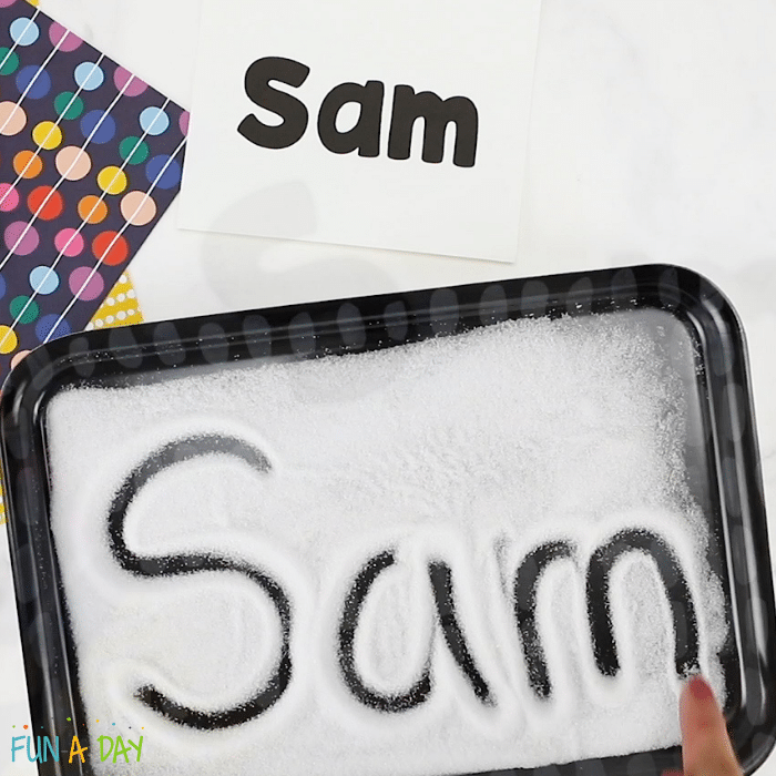 a card with the name Sam on it above a salt tray with a finger writing the name Sam