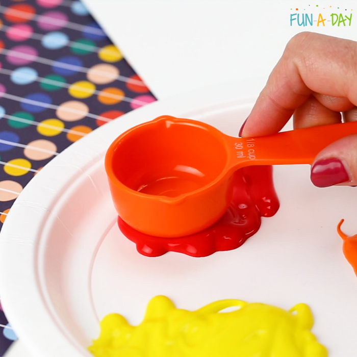a measuring cup being pressed into orange paint to use in circle art