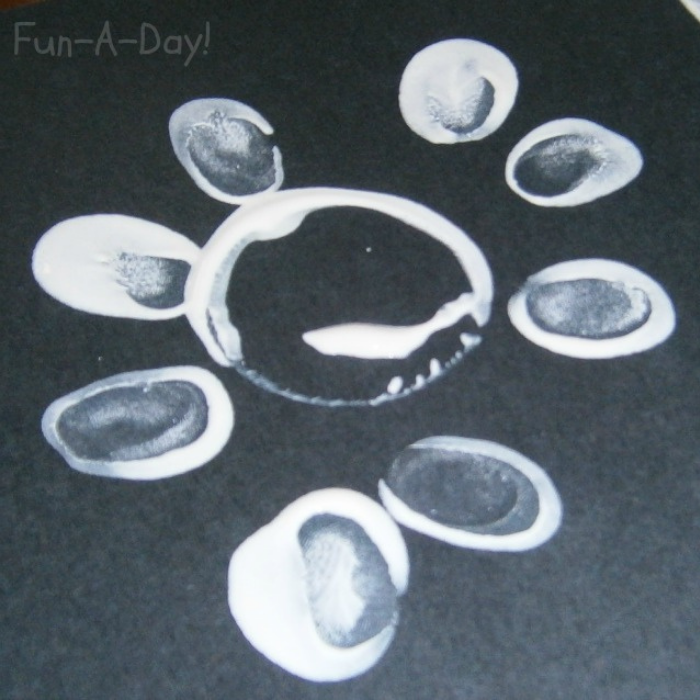 white fingerprints making flower petals around a while circle on black construction paper