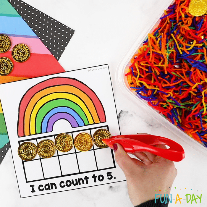 a rainbow ten frame printable that reads 'I can count to 5' and a hand putting five gold coins onto it 
