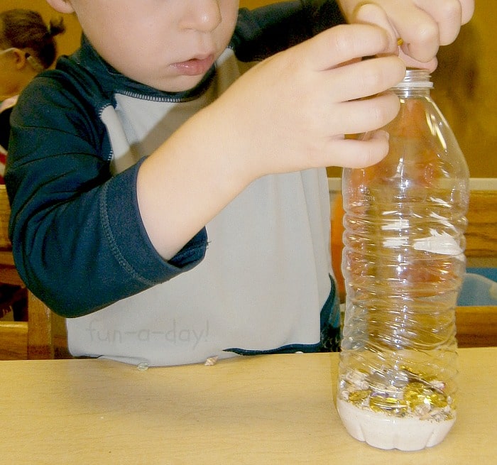 child adding craft gems to a sensory bottle