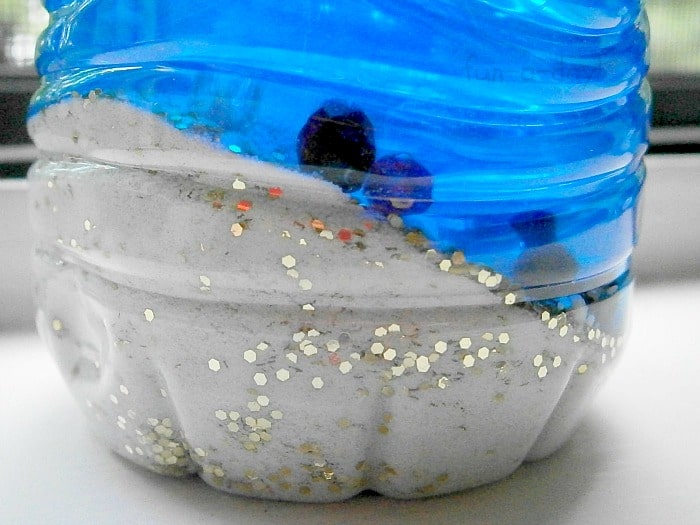 closeup of the bottom of a pirate sensory bottle with sand, craft beads, and blue-tinted water