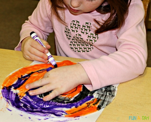 a preschool girl coloring a colorful coffee filter with a purple marker