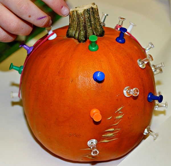 Preschooler adding rubber bands to a pumpkin geoboard made with pumpkin and push pins