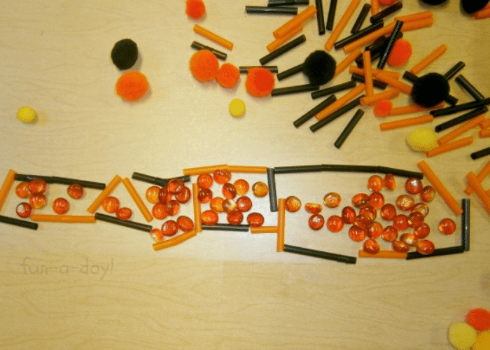 Preschool contact paper art using orange and black loose parts.