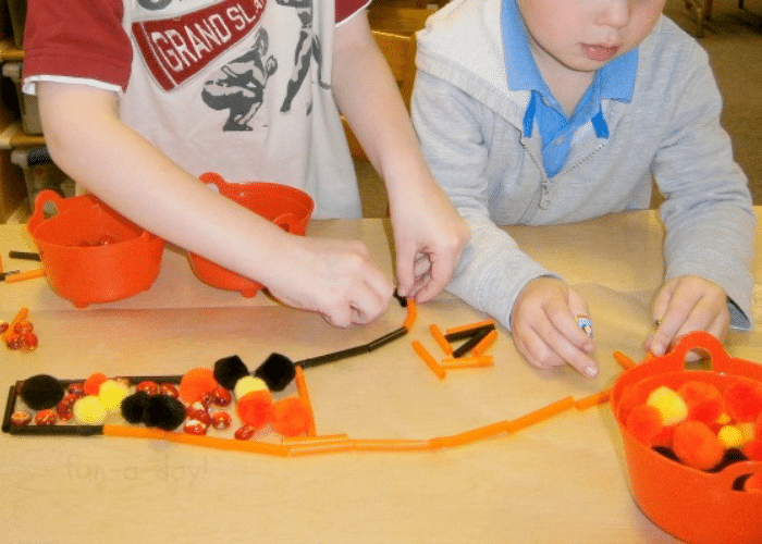 Two preschoolers creating Halloween contact paper art with loose parts and sticky paper.