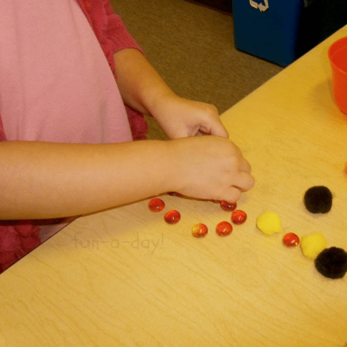 Preschooler placing orange glass gems and pompoms on contact paper.