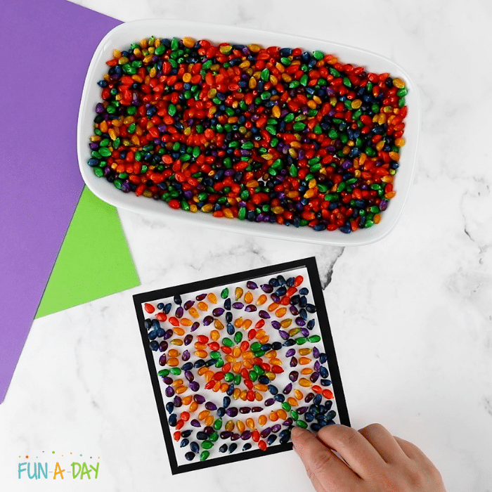 a tray of dyed popcorn kernels and a square colorful corn mosaic