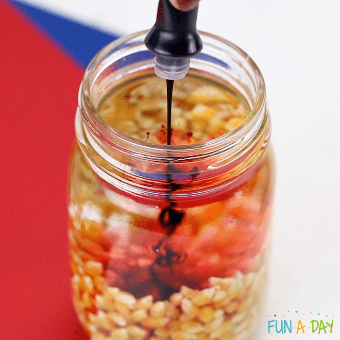image of popcorn kernels in a glass jar with food coloring being added