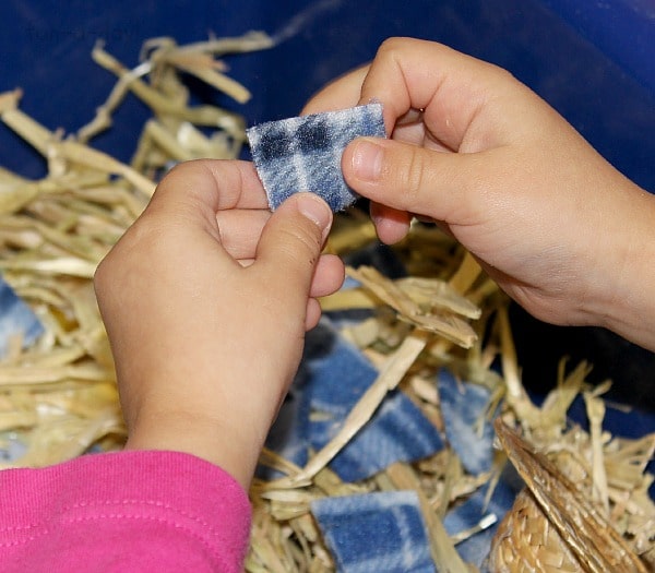 Child's hand holding flannel square over scarecrow sensory bin.