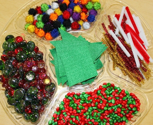 Round sectioned tray with green felt, colorful pompoms, pipe cleaner pieces, red and green glass gems, and red and green corn kernels