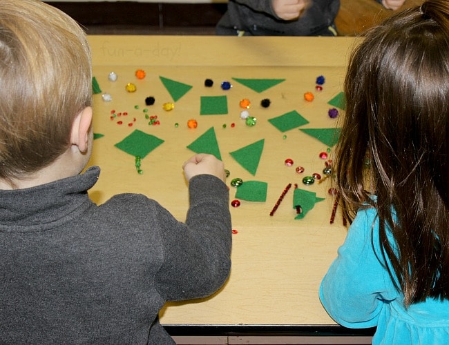 Two preschoolers placing Christmas-themed loose parts on contact paper to create art.