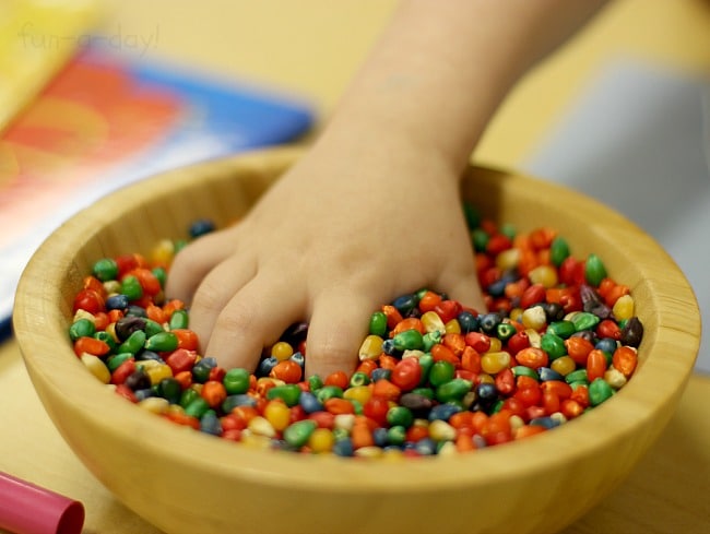 Preschooler's hand in a bowl full of dyed rainbow corn.