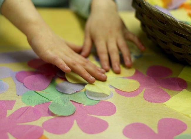 child's hands placing tissue paper flowers onto tissue paper stained glass art