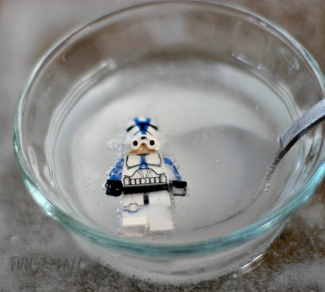 Spoon scooping LEGO stormtrooper out of small glass bowl full of liquid