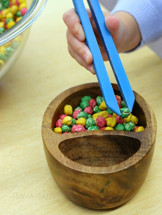 preschooler using child tweezers to pick up sensory materials in apple sensory bin