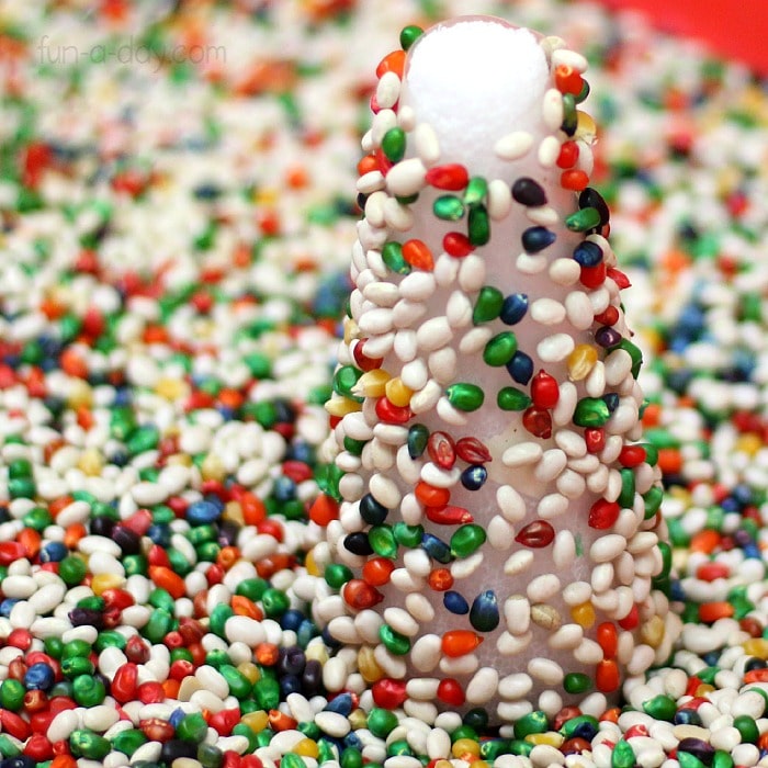 Preschool sensory bin filled with white beans, colored corn kernels, and sticky christmas tree.