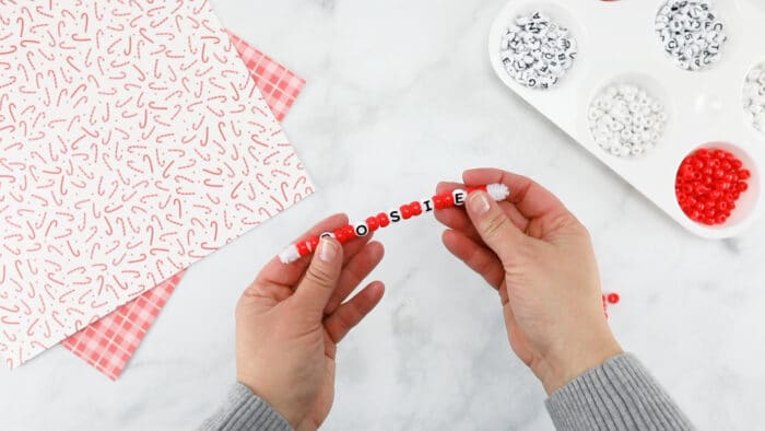 hands holding a pipe cleaner filled with a pattern of red beads and white beads spelling the name rosie