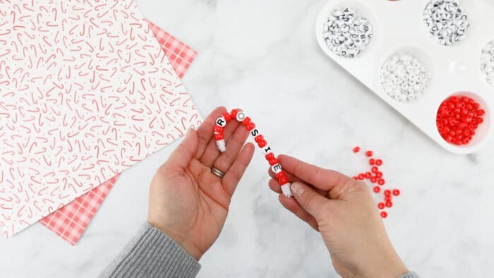 hands holding a pipe cleaner with red and white beads bent into a candy cane shape