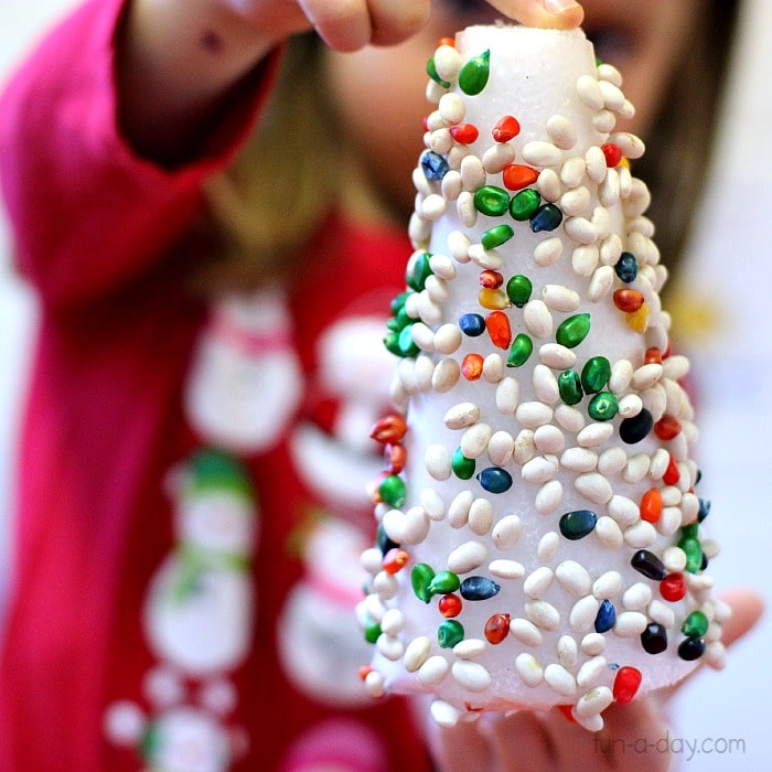 Preschooler holding a 3D contact paper christmas tree covered with beans and colored popcorn.
