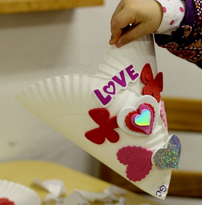 child's hand holding homemade paper plate valentine holder