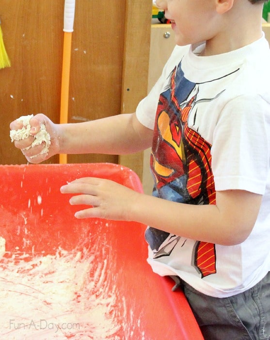 a preschool boy gleefully squeezing a handful of fake snow made with flour