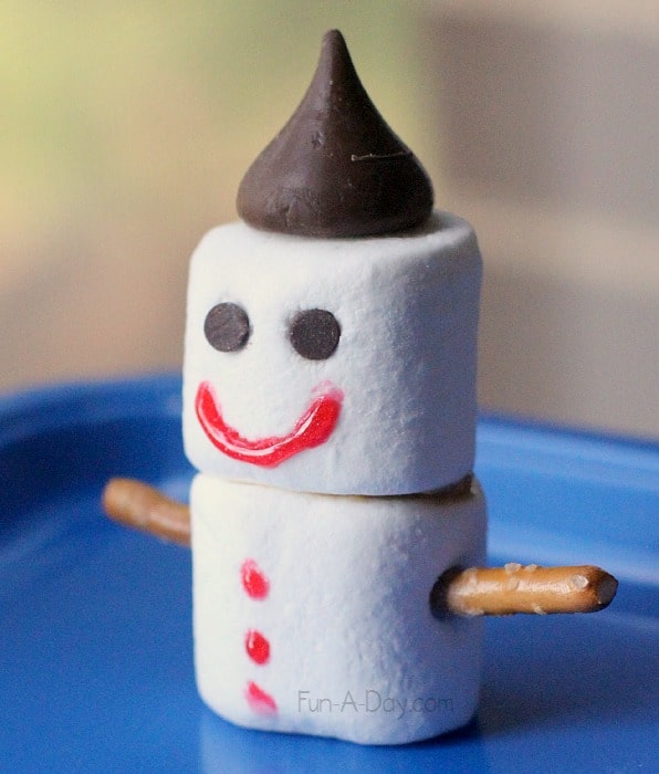 two marshmallows stacked together with a Hershey's kiss hat and pretzel arms and an icing face that looks like a snowman