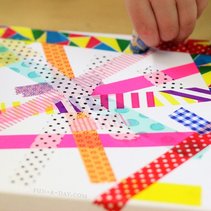 Child's hand placing colorful tape on a white canvas.