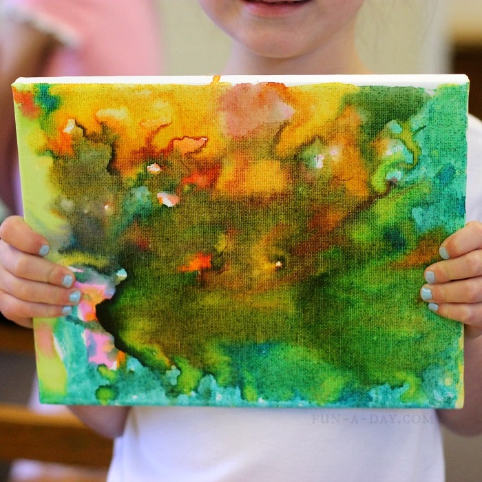 Child holding a canvas painted with liquid watercolors.