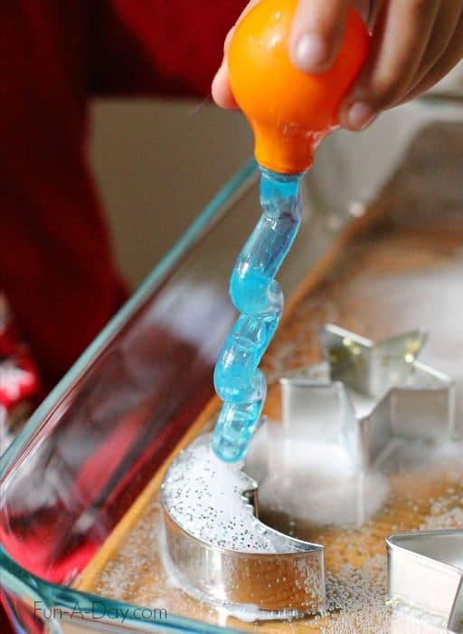 Child squeezing vinegar onto baking soda in moon and star cookie cutters.
