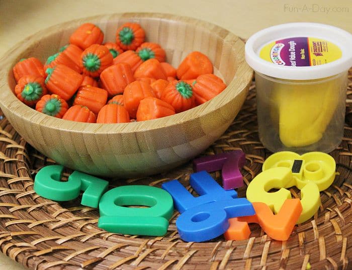 bowl of candy pumpkins, yellow play dough, and magnetic numbers on a tray