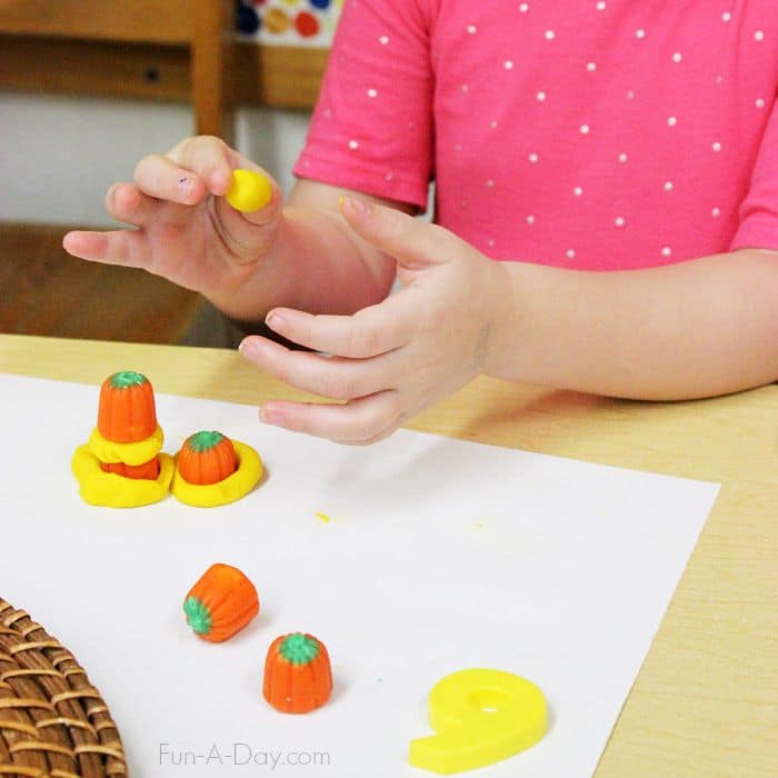 child building with yellow play dough and pumpkin candy during a pumpkin math and engineering challenge