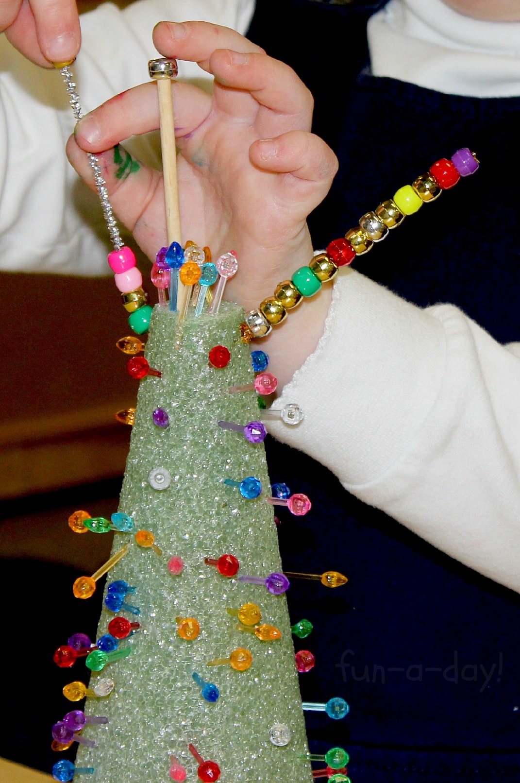 Child adding beads and lights to a styrofoam tree