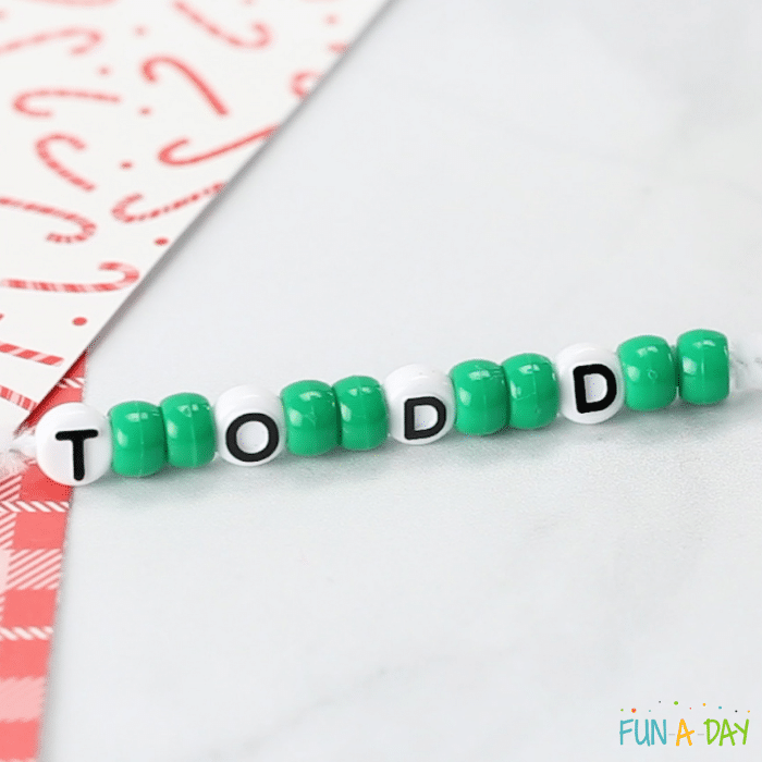 Green pony beads on a pipe cleaner, along with letter beads that spell Todd. Part of the beaded wreath creation process.