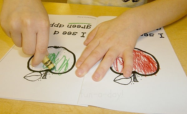 child coloring in an apple book with a green crayon