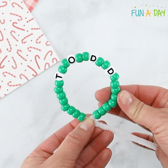 Making a wreath ornament with green pony beads and letter beads on a pipe cleaner.