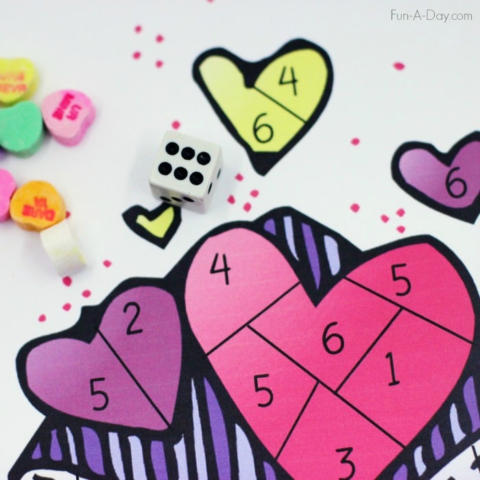 close up of a heart game divided into different numbers, a die, and candy hearts used in the game 