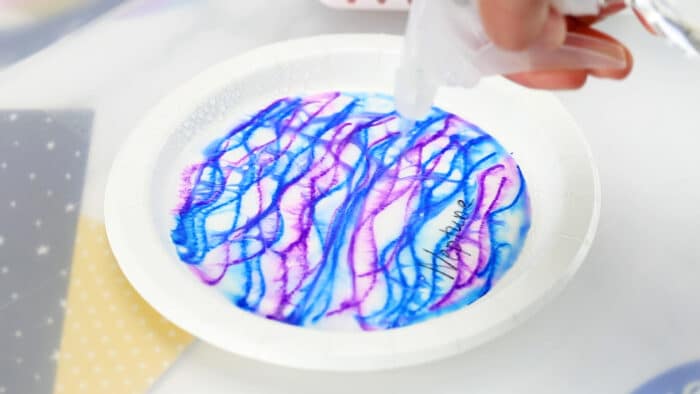 spray bottle of water spraying a coffee filter covered in blue and purple lines to look like neptune