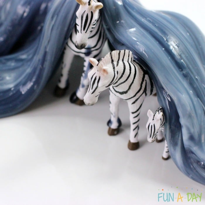 Three zebras under a black and white striped zebra slime that has mixed to turn grey