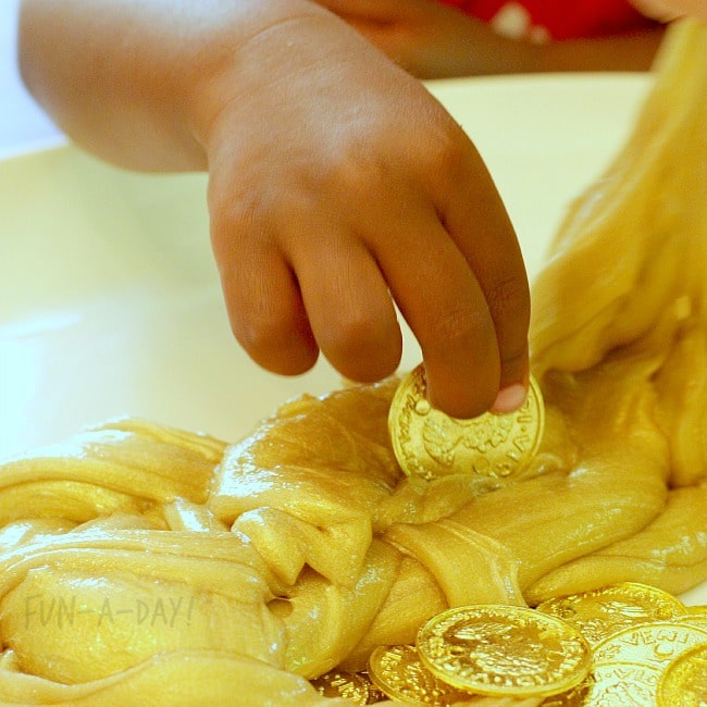 Child's hand placing plastic gold coins into gold slime