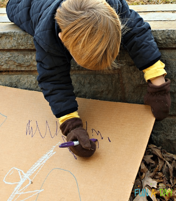 Preschooler drawing on cardboard box with permanent marker.