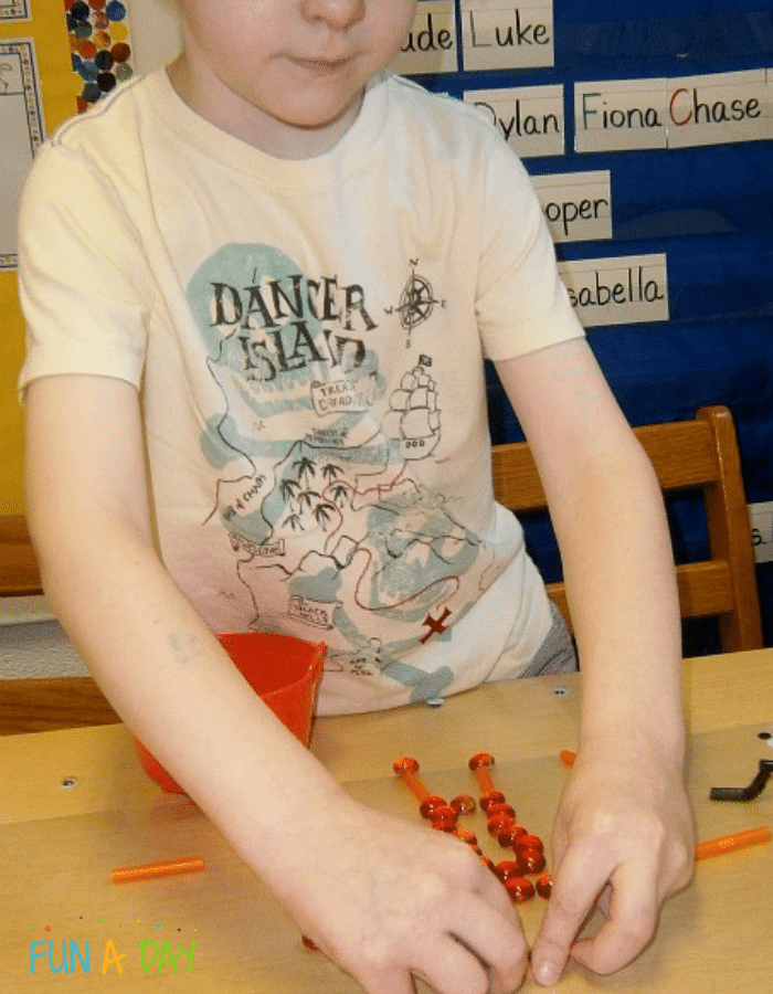 Child making transient art with glass gems and straws on contact paper