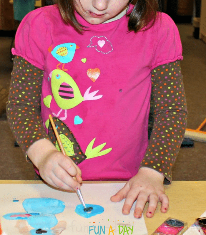 Preschool child using watercolors to paint on white paper.
