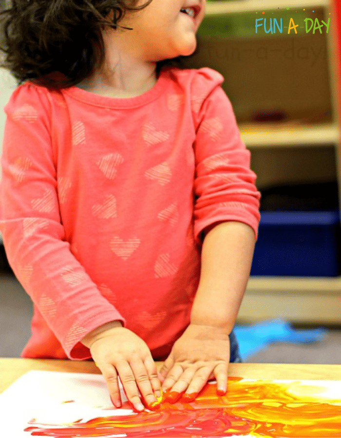 Child using hands to mix yellow and red paints