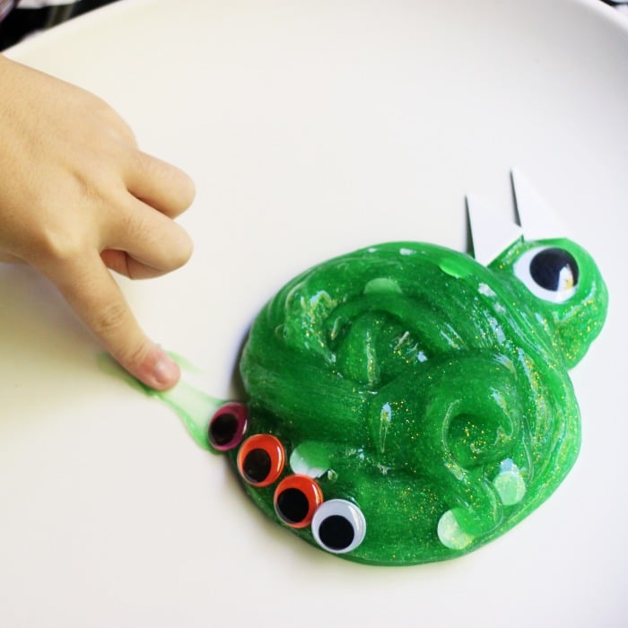 child's finger poking at green slime with googly eyes