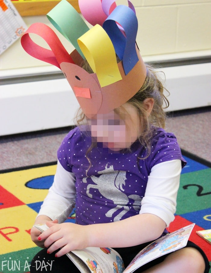 Preschool child reading while wearing turkey hat craft.