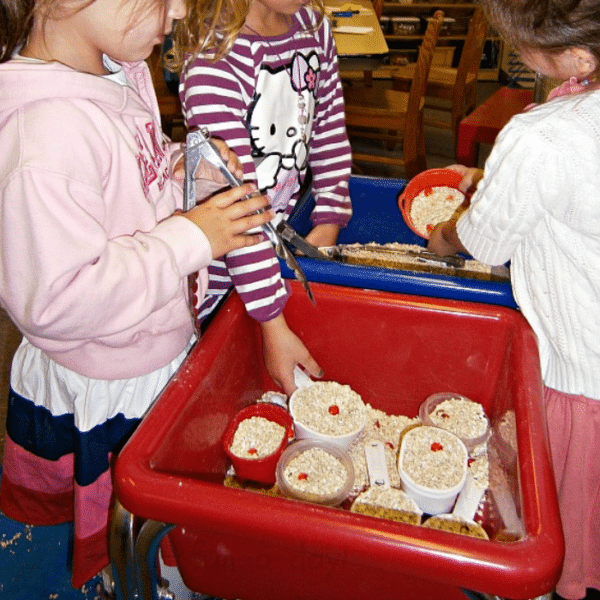 Three children using a sensory bin filled with oats and orange glass gems.