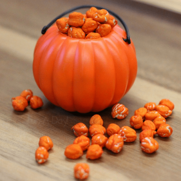 Orange dyed chickpeas in and around small plastic pumpkin pail