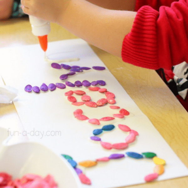 Child gluing colorful pumpkin seeds to white paper to make her name.