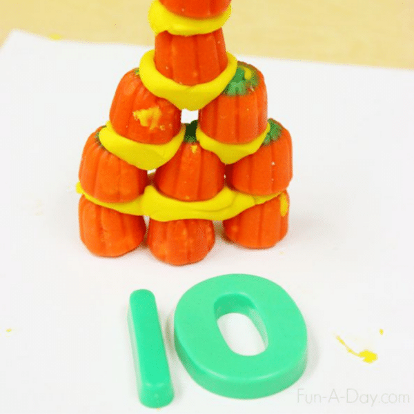 Ten candy pumpkins stacked together with yellow play dough, with magnetic numbers 1 and 0 in front.
